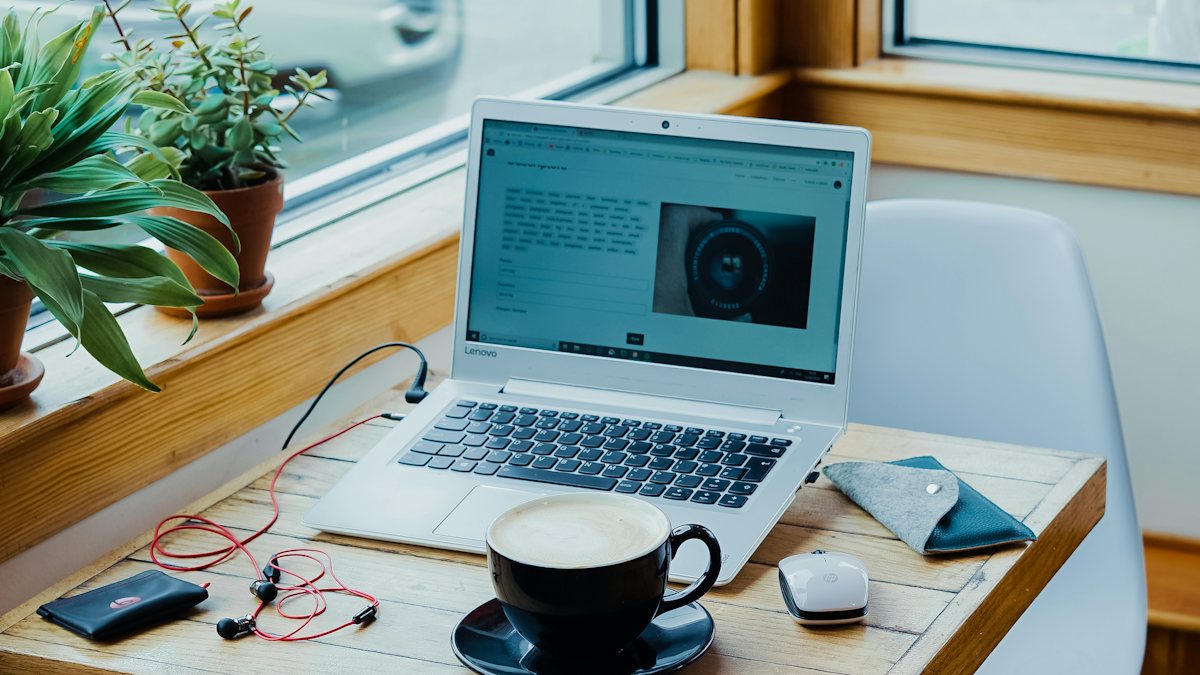 A laptop, coffee and earphones on a wooden table