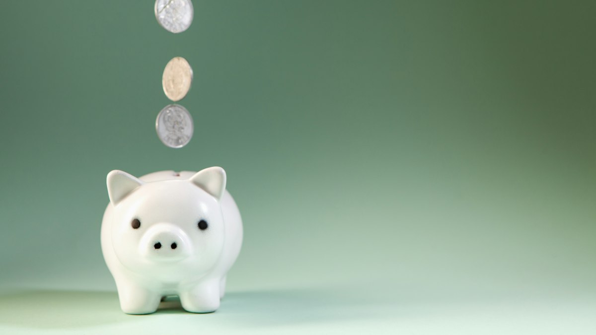 Coins dropping into a white piggy bank