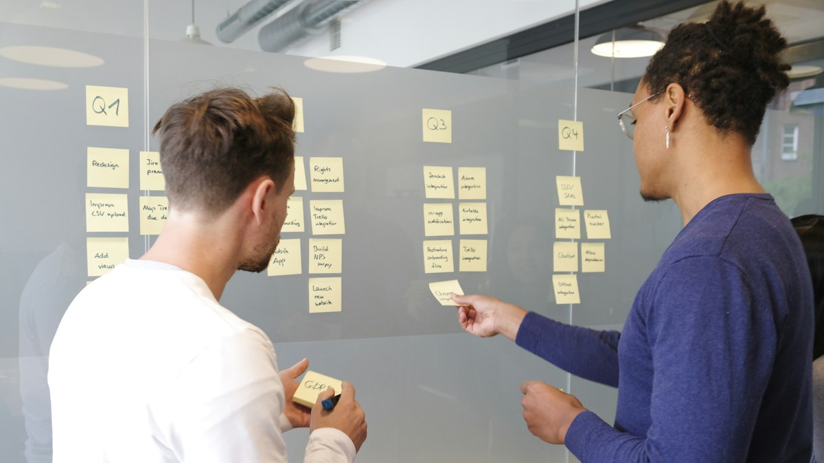 Two people planning a project with sticky notes on a glass wall