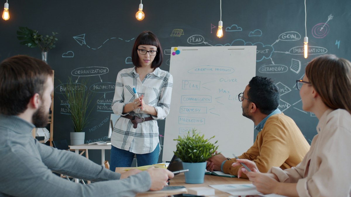 A woman presenting to colleagues at a whiteboard